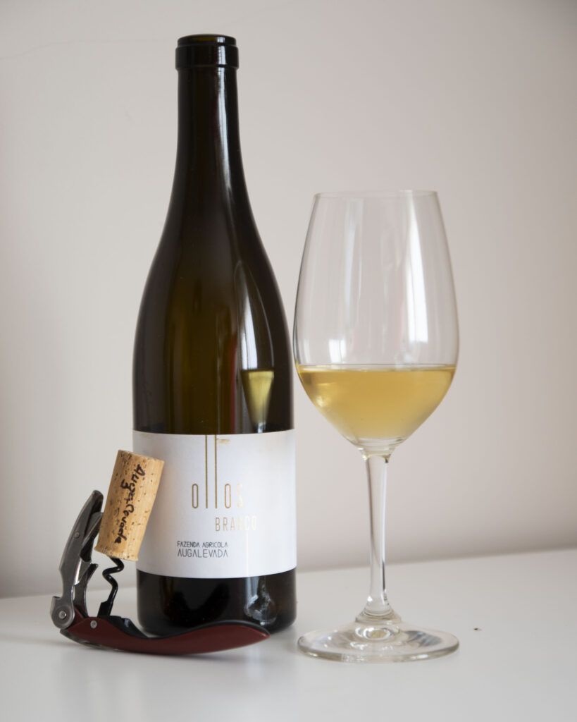 Botella de Ollos Branco 2022, con una copa del vino servida y un sacacorchos con el corcho de la botellas.