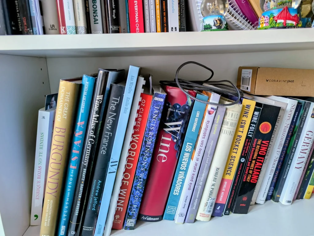 Una estantería de madera blanca llena de libros sobre vino, con títulos como 'The Great Domaines of Burgundy' y 'Jancis Robinson's Wine Course'.