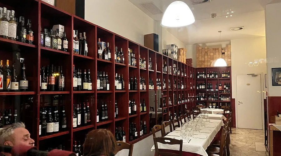Interior de una enoteca con largas estanterías de madera repletas de botellas de vino y una mesa alargada preparada para una cata.