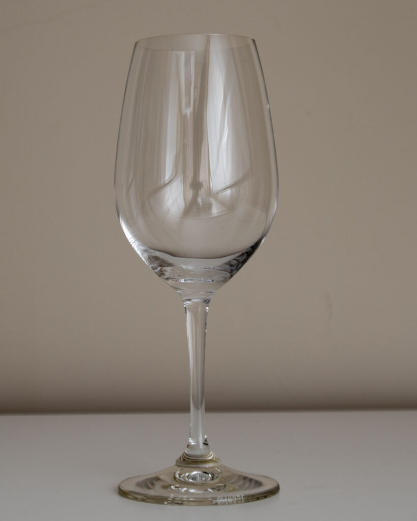 Primer plano de una copa de vino transparente de tallo largo y cáliz de tulipa, sobre fondo neutro.