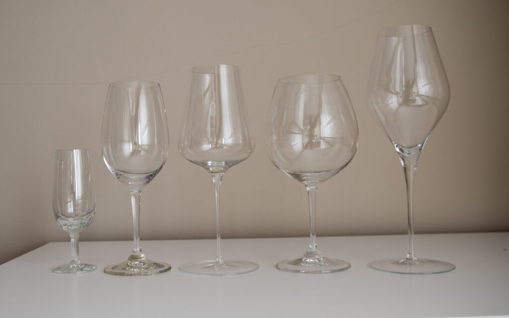 Una hilera de cinco copas de vino de diferentes formas y tamaños, desde una copa flauta estrecha hasta una copa de tulipa muy ancha.