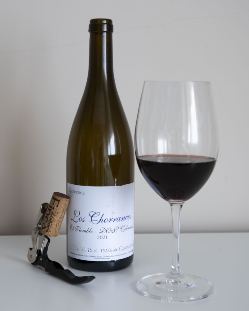 Botella de vino Los Chorrancos 2021 de Daniel Ramos junto a una copa de vino tinto servida y un sacacorchos con corcho.