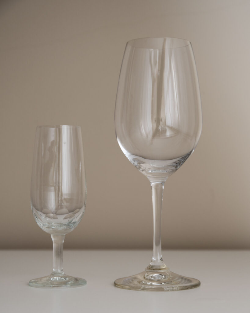 Dos copas de vino sobre una mesa blanca: una copa pequeña y estrecha tradicional junto a una copa grande de tulipa para vino blanco.