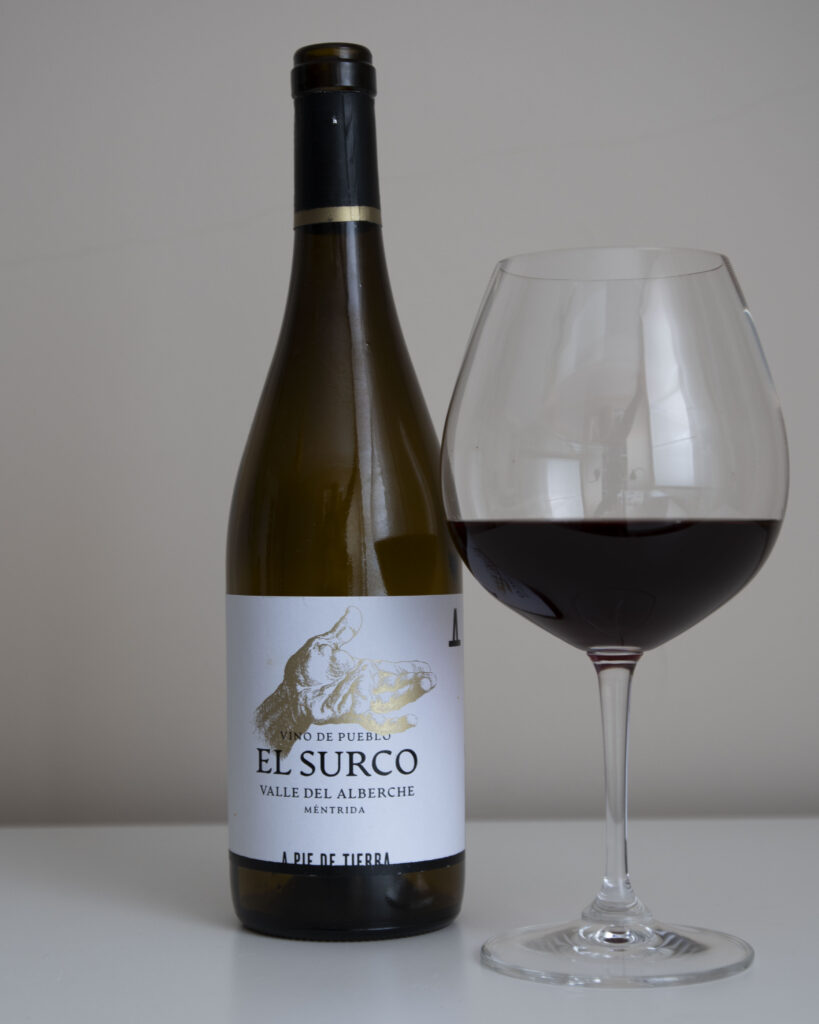 Botella de vino tinto o blanco 'El Surco 2022, Valle del Alberche Méntrida' de A Pie de Tierra, junto a una copa de vino tinto servida.