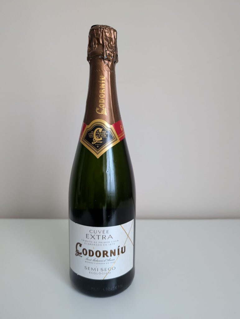 Botella de Cava Codorníu Cuvée Extra Semi Seco Ecológico, espumoso con cápsula dorada y etiqueta blanca y roja, sobre fondo neutro.