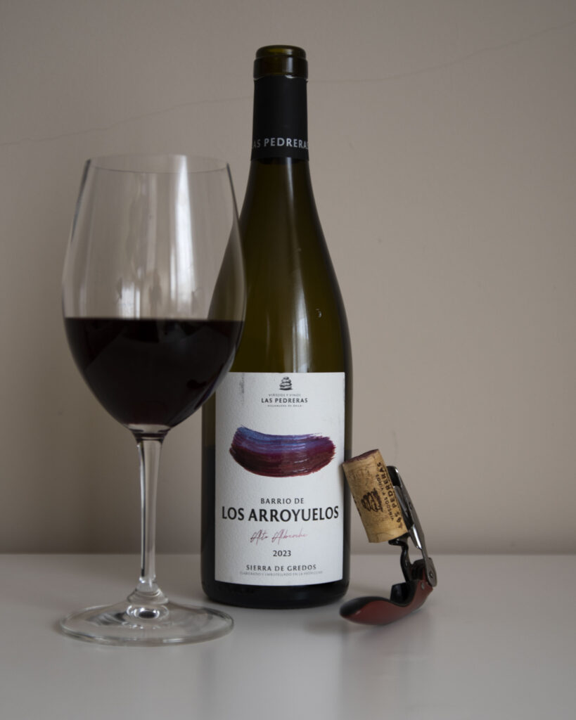 Botella de Barrio de los Arroyuelos 2023 con copa de vino tinto servida y sacacorchos sobre fondo neutro.