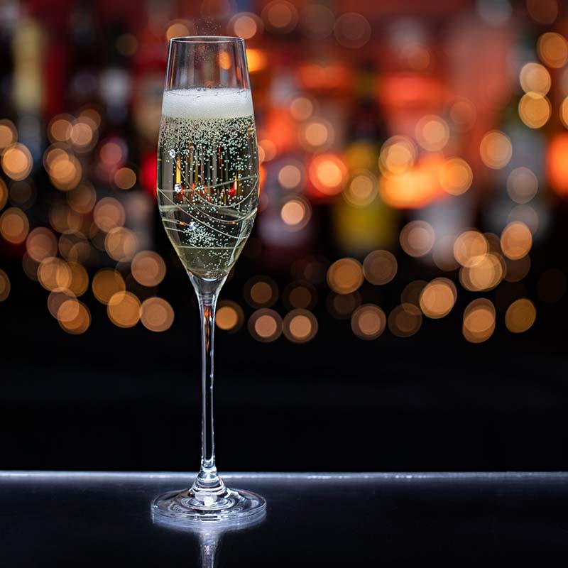 Copa alta de champagne con burbujas finas sobre un fondo desenfocado de luces.