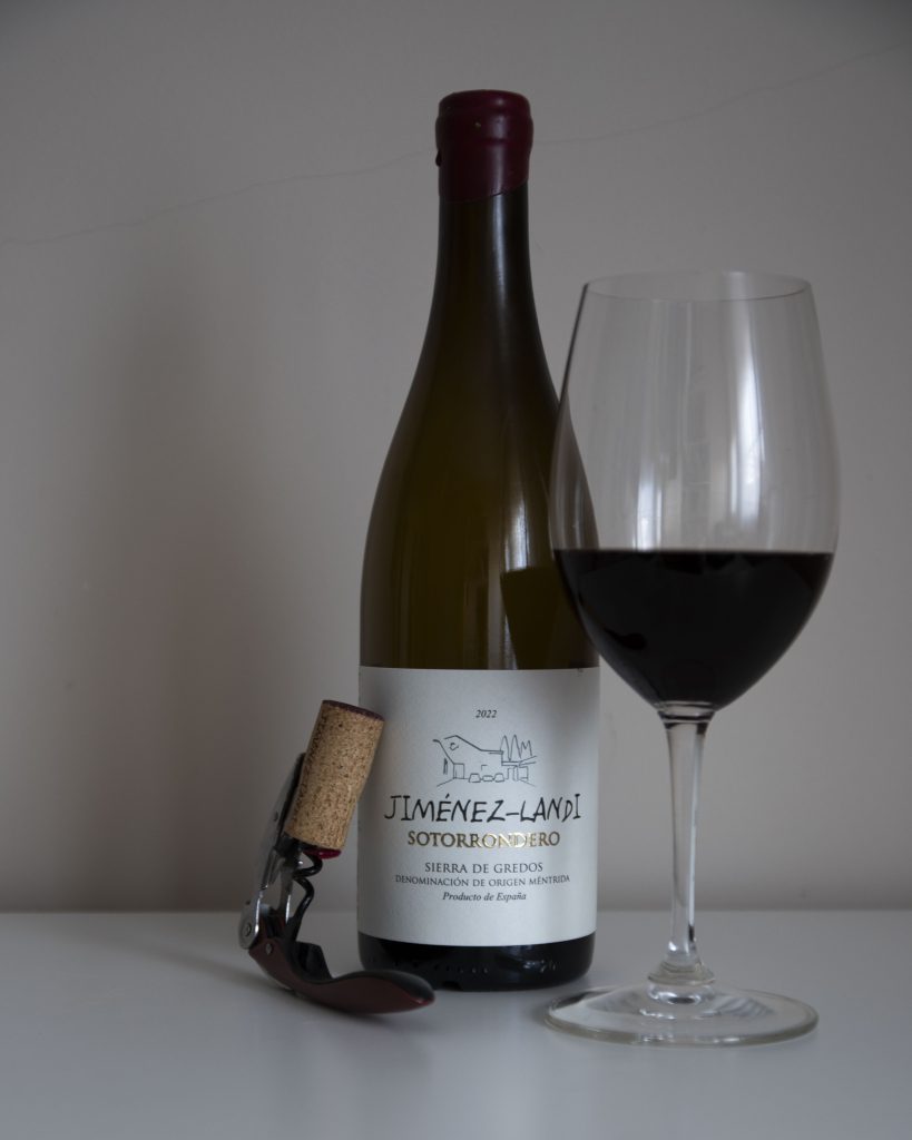 Botella de Sotorrondero 2022 de Jiménez‑Landi junto a una copa de vino tinto servida sobre una mesa blanca.