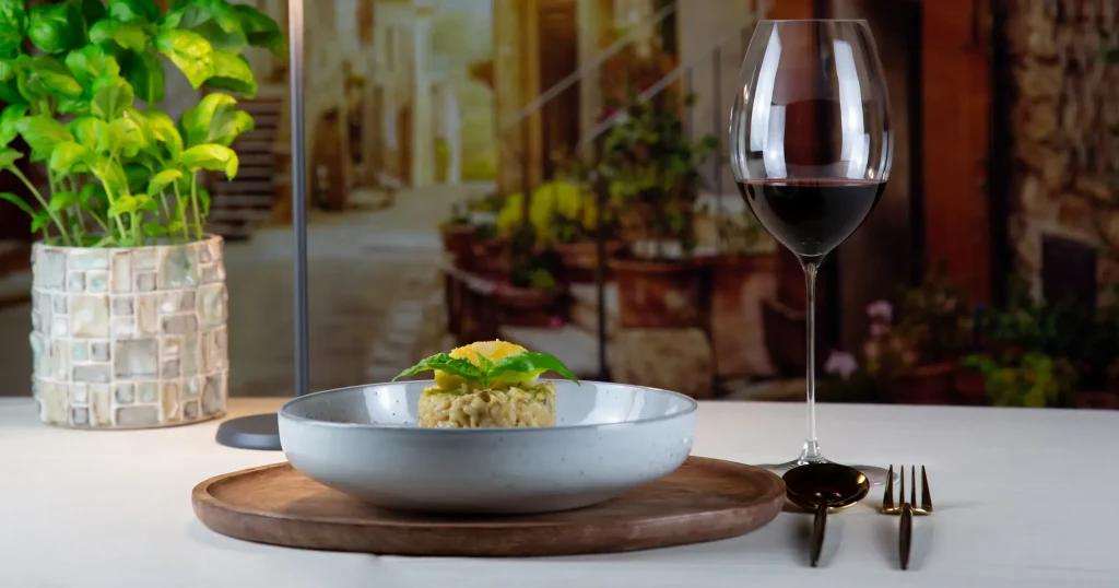 Copa de vino tinto en una mesa con plato de comida en un ambiente mediterráneo relajado.