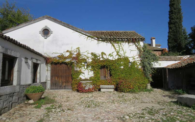 Fachada de una bodega rural encalada con patio empedrado y vegetación trepadora.
