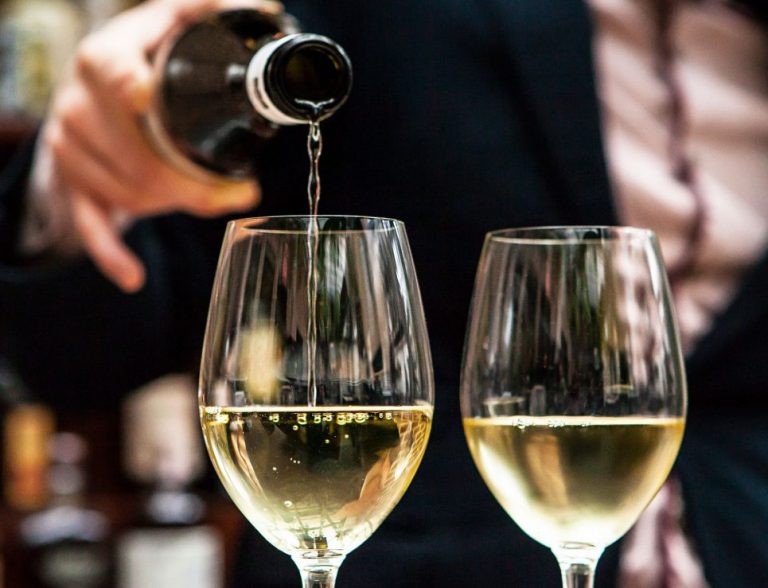 Persona sirviendo vino blanco en una copa durante una cata.