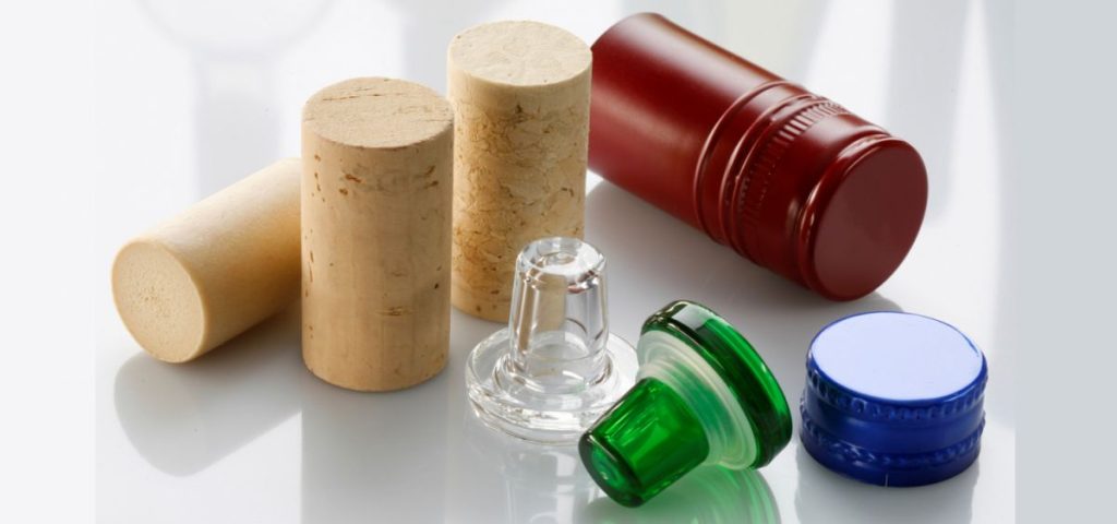 “Varios tipos de cierre para botellas de vino: corchos naturales, tapones sintéticos, de vidrio y de rosca sobre fondo blanco.”