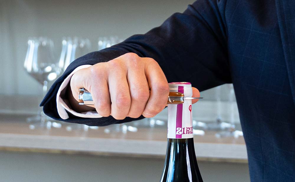 Mano sujetando un sacacorchos de camarero mientras descorcha una botella de vino en una barra.