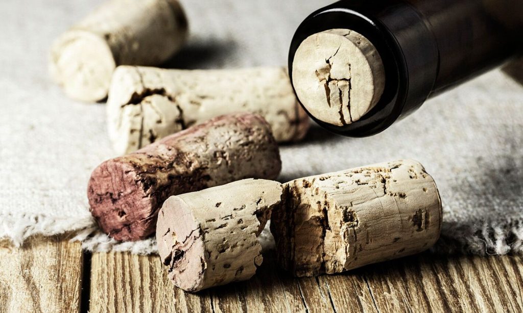 Varios corchos de vino usados sobre una mesa de madera, algunos manchados y dañados junto al cuello de una botella.